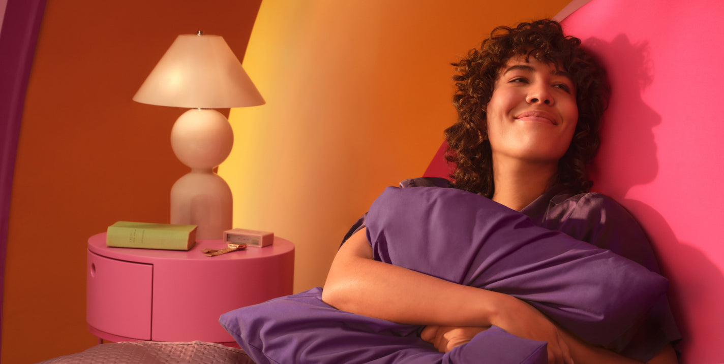 Smiling woman tucked into her bed hugging a pillow
