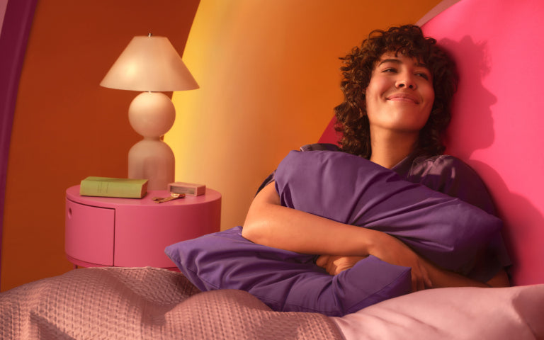Smiling woman tucked into her bed hugging a pillow